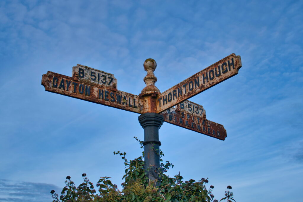 An old, rusting sign showing directions to Gayton, Heswall, Thornton Hough and Birkenhead in Wirral, UK